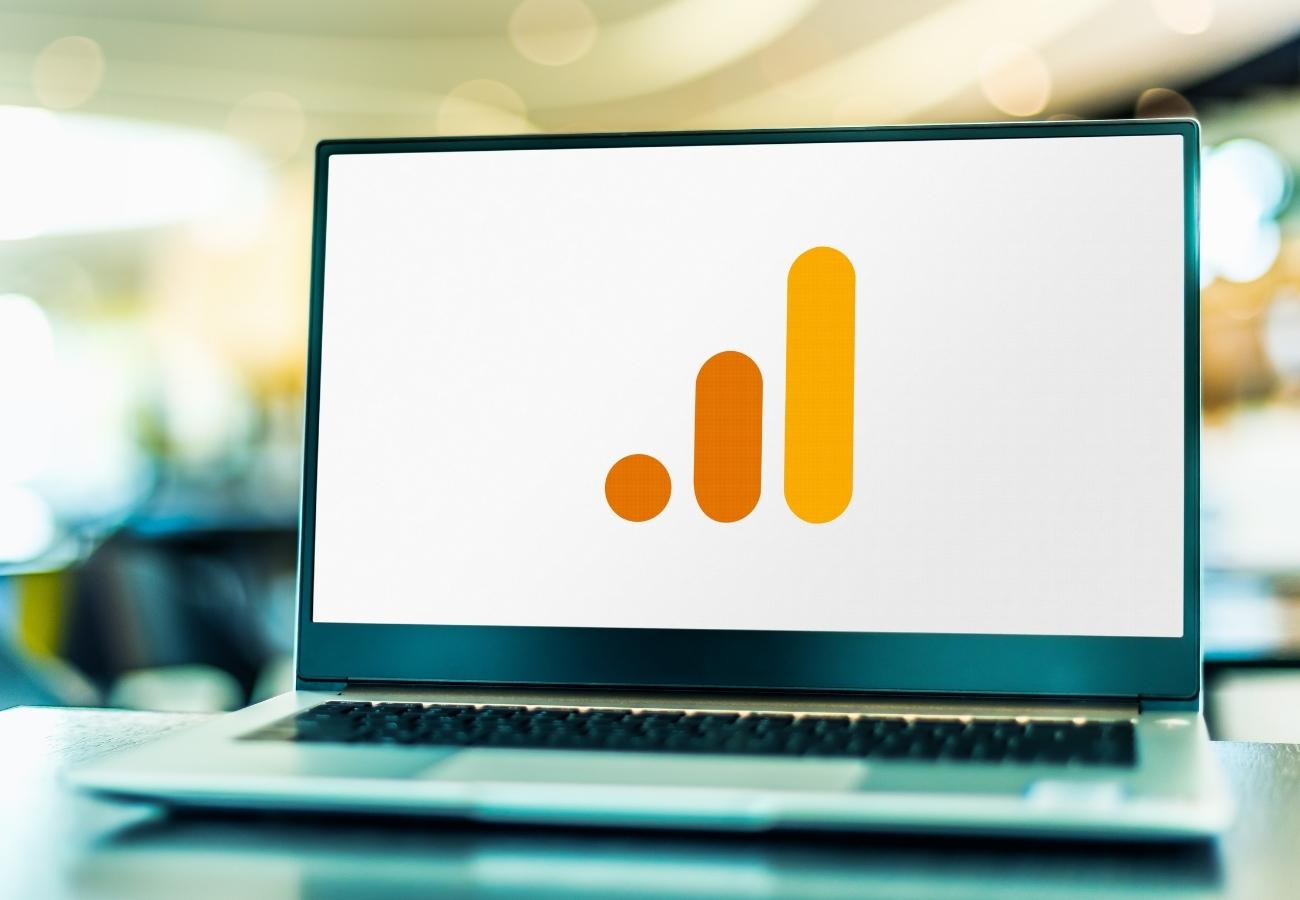 Kannettava tietokone pöydällä, näytössä Google Analyticsin oranssi logo